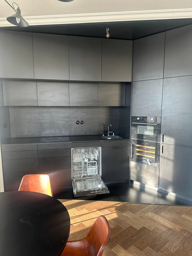 A grey-and-black kitchen with wipe marks on the matte surfaces and an open dishwasher.