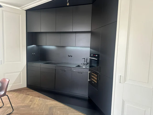 The same grey-and-black kitchen from a different angle, with the dishwasher closed and the under-cabinet lights on.